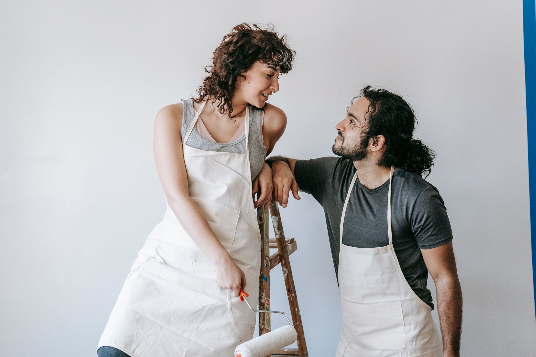 Smiling couple in aprons painting a wall with a roller, enjoying the renovation process in Temecula, CA