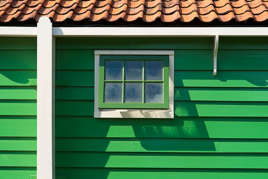 Green painted wooden house wall with a small window